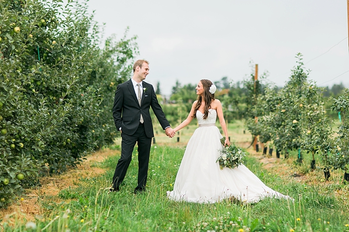 Bride and groom standing at an apple orchard, holding hands and looking at each other smiliming