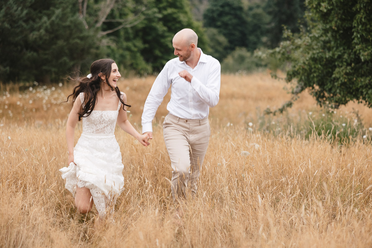 Couple joyfully running through a golden field at their Vashon Island wedding.