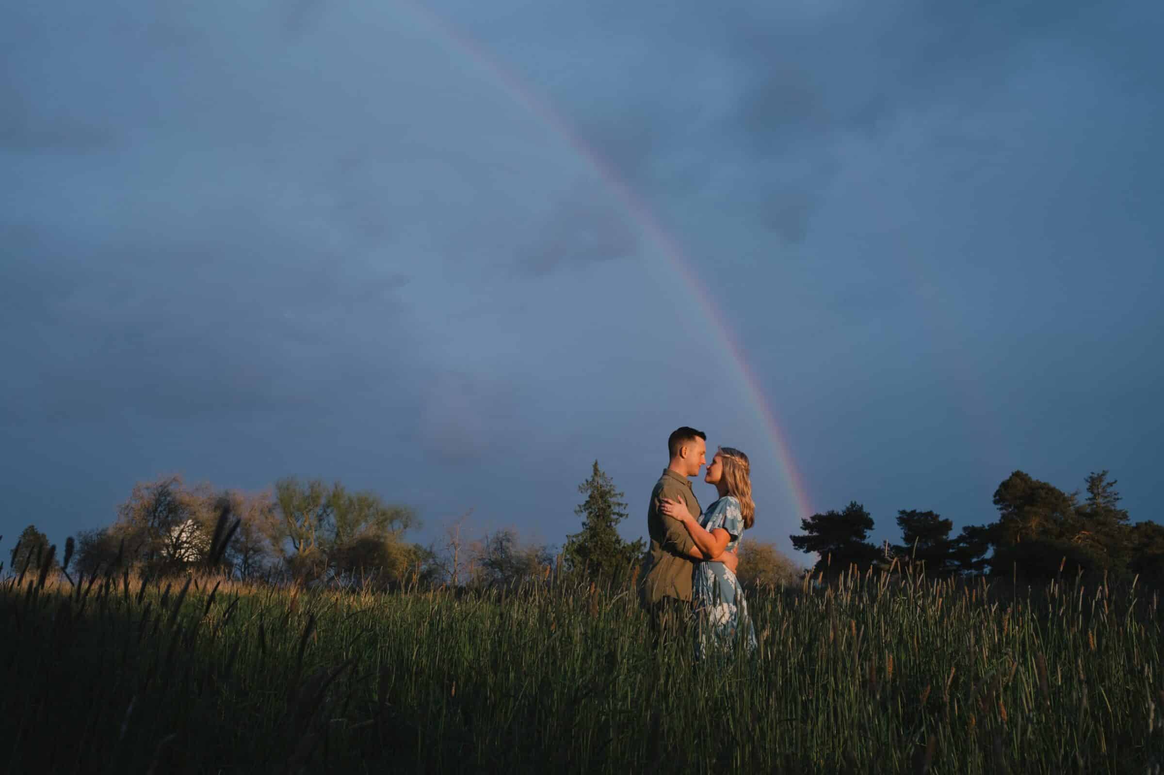 Engagement photo in Discovery Park Seattle in the grassy field and rainbow visible in the distance.
