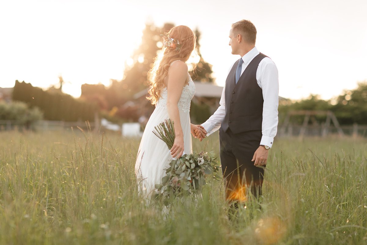 Bride and groom standing in a grassy null at sunset.
