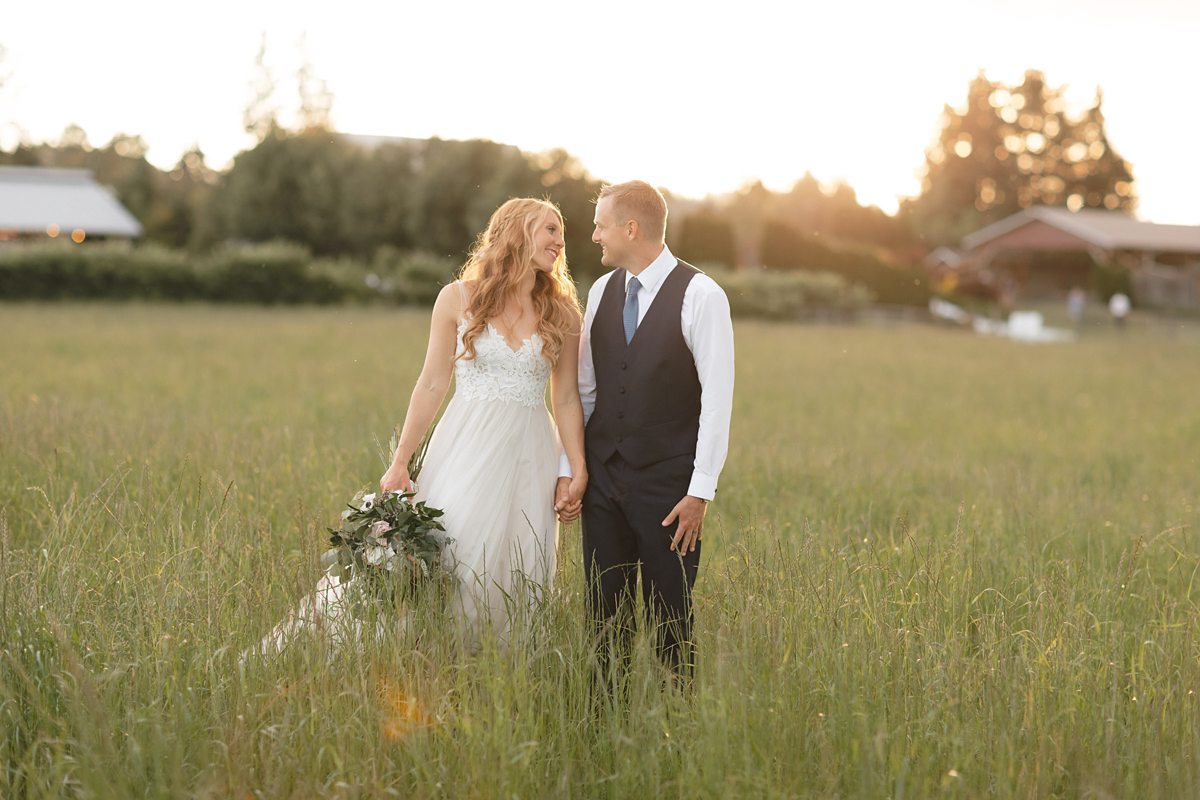 Happy bride and groom standing in a field at sunset during their Snohomish wedding at Swans Trail Farms.