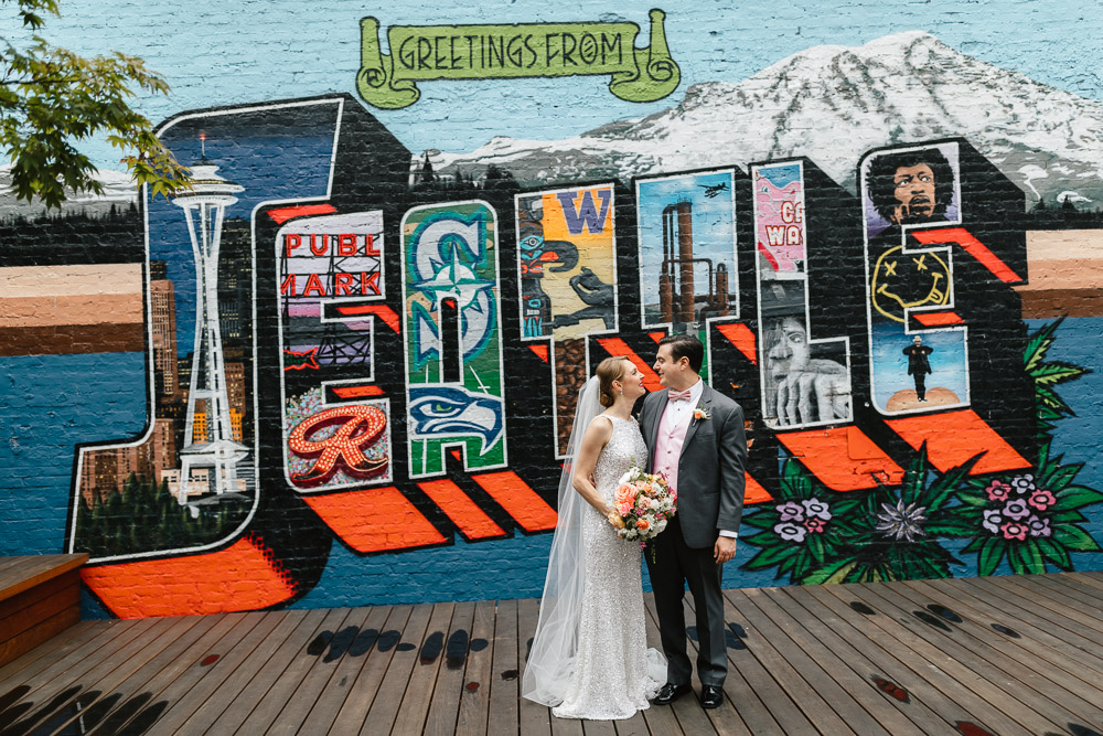 Couple posing before Seattle-themed mural in the courtyard of Block 41 on wedding day.