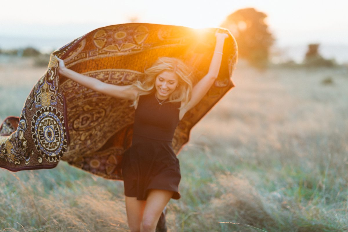 Woman twirling with patterned scarf at sunset in field.