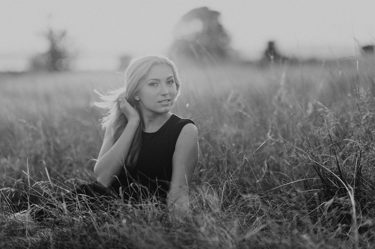 Young woman sitting in a grassy field in Discovery Park Seattle in a black dress.