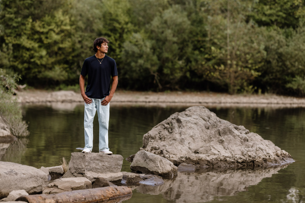 Young man standing on rocks by tranquil lake.