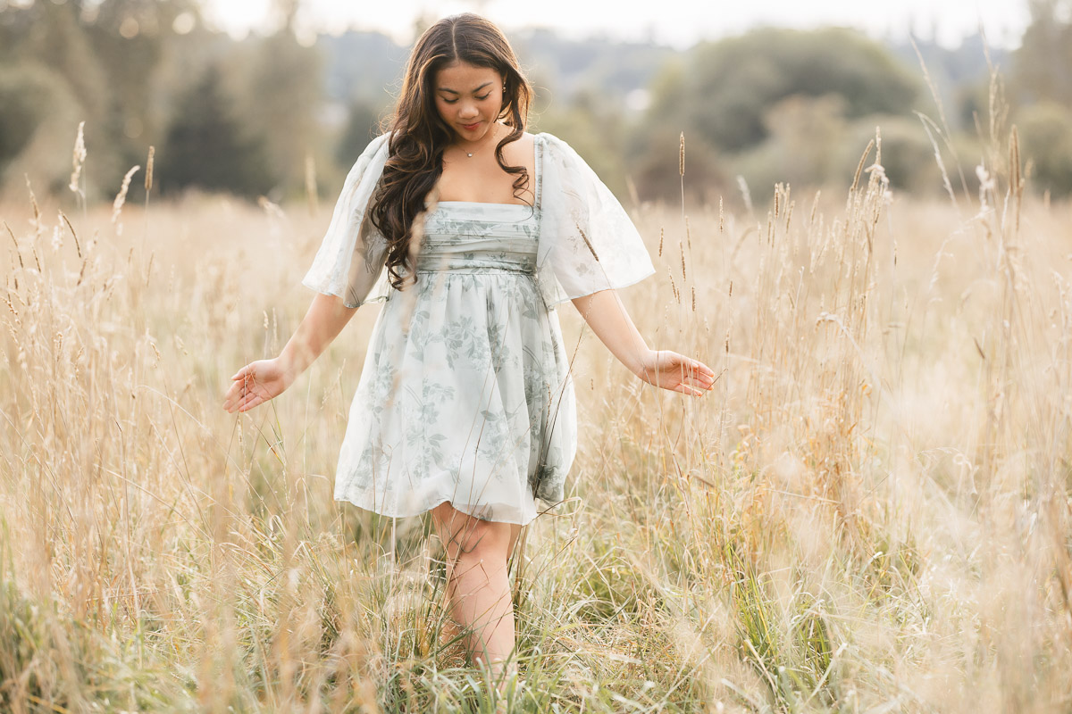 High school senior strolling through sunlit meadow in floral dress