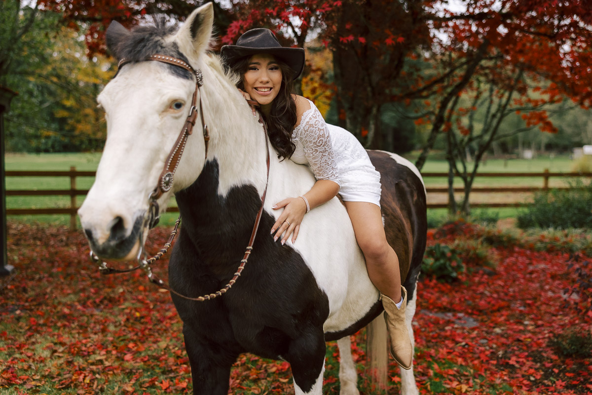 Young woman in white dress riding horse in autumn at a paddock.