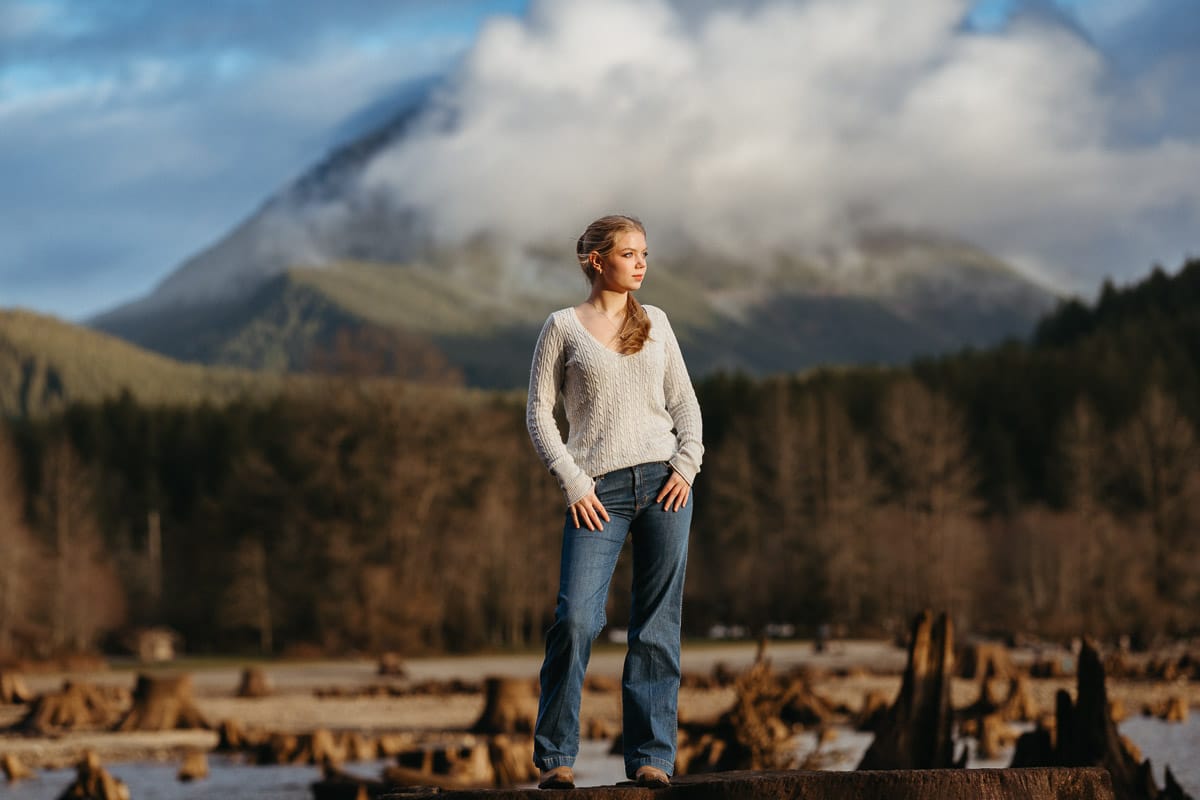 High school senior standing on a tree stump with a mountain in the background